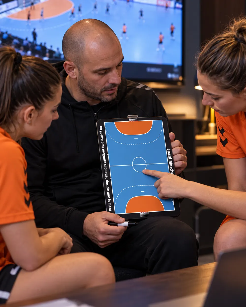Un entrenador de balonmano repasa la táctica con la pizarra junto a sus jugadoras